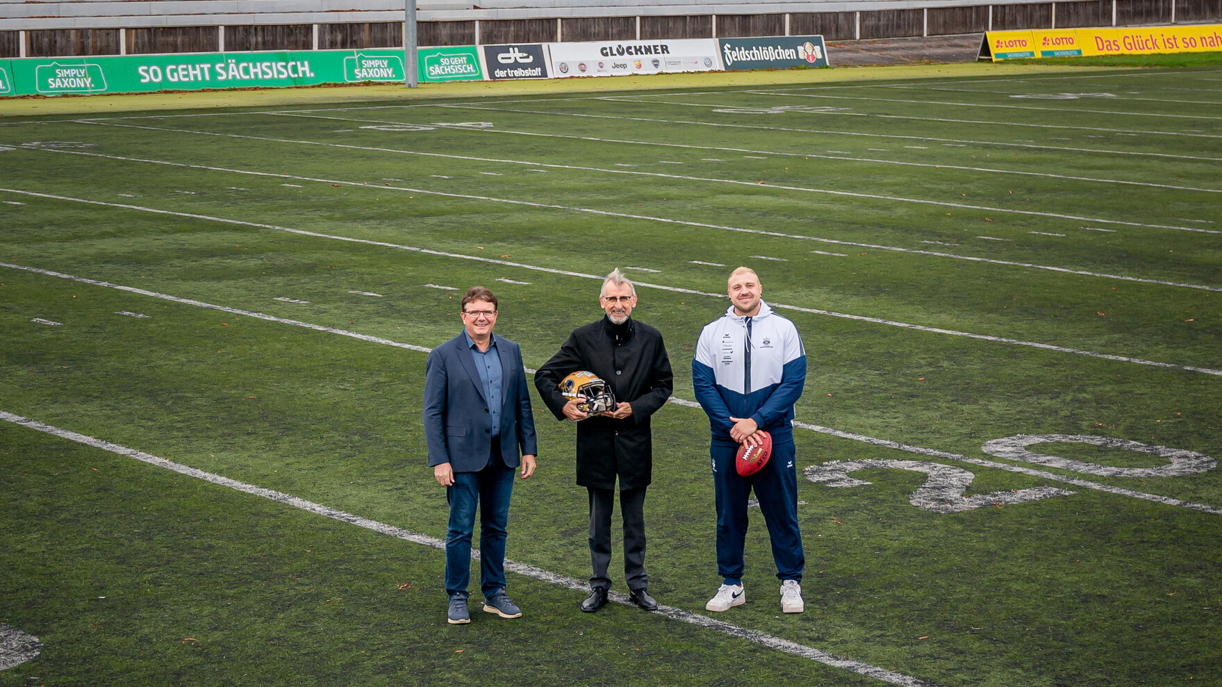 Drei Männer stehen auf einem Football-Feld und posieren für ein Foto.
